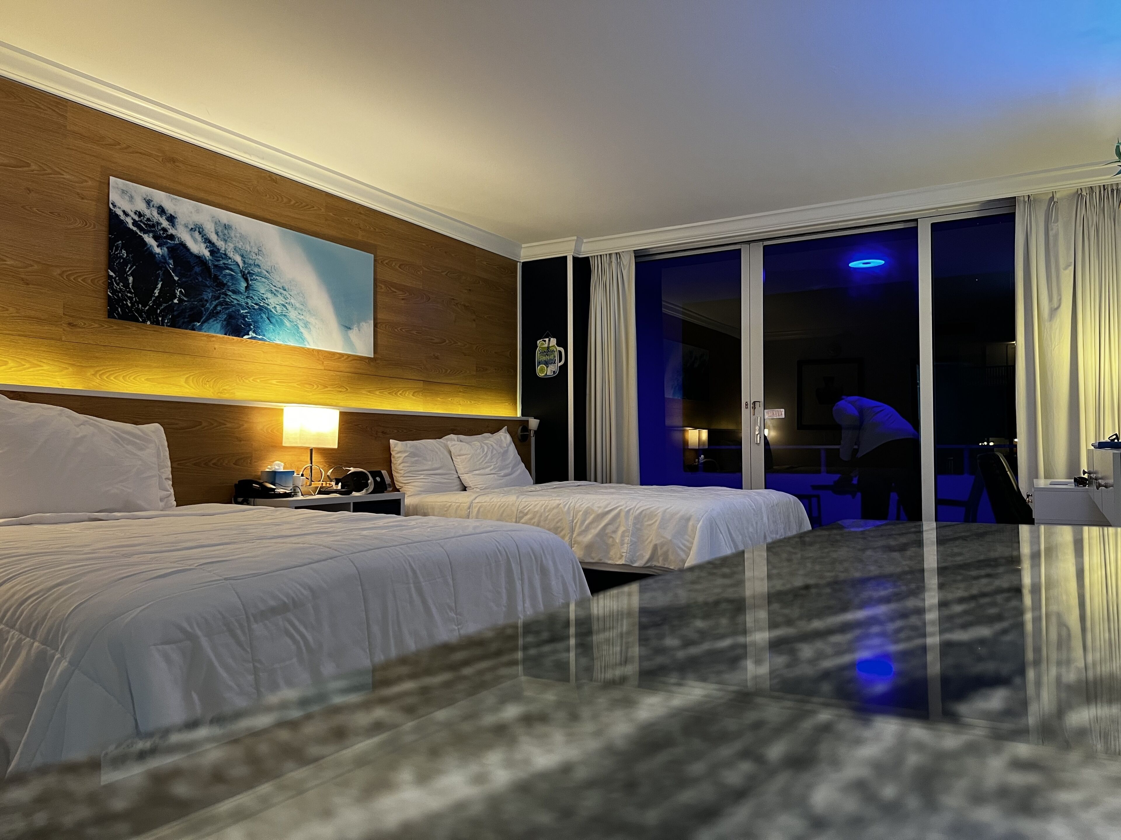 A hotel room with two beds, a large painting on the wall, and a view of the outside balcony.