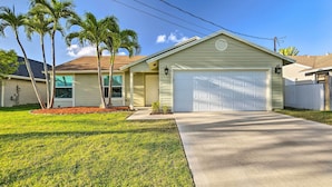 A single-story house with a white garage, a covered porch, and a well-maintained lawn with palm trees.