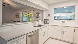 A modern kitchen with white cabinetry, a built-in dishwasher, a large window with a view, and a coffee machine.