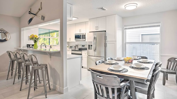 A modern kitchen with white cabinets, stainless steel appliances, and a dining area with a wooden table and metal chairs.