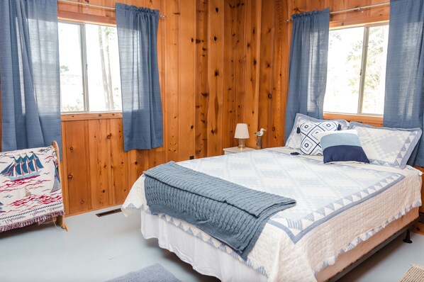 A wooden-paneled bedroom with a bed, curtains, a lamp, and a chair.