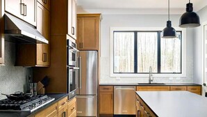Una cocina moderna con armarios de madera, electrodomésticos de acero inoxidable, un amplio ventanal e iluminación colgante.