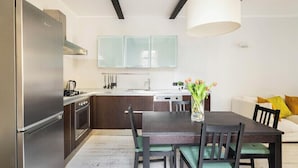 A modern kitchen with a stainless steel refrigerator, dark wooden cabinets, a white countertop, and a dining table with chairs.