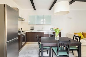 Una cocina moderna con un refrigerador de acero inoxidable, armarios de madera oscura, una encimera blanca y una mesa de comedor con sillas.