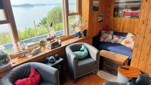Een knus vakantiehuisje met houten inrichting, een bank, twee fauteuils, een bijzettafeltje en uitzicht op een meer.