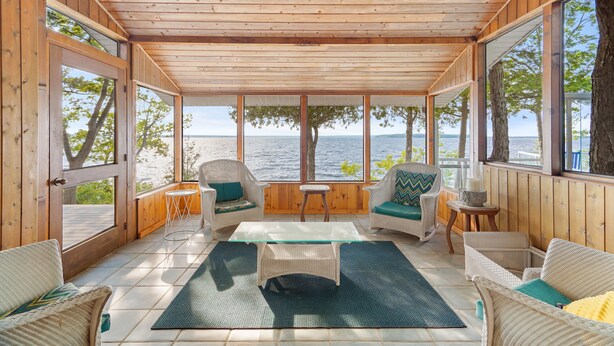 A wooden-paneled room with a glass table, wicker chairs, and a view of the sea. - Beautiful Luxury Lake Front Cottage Georgian Bay (Georgian Bay)