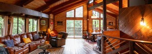 A cozy cabin interior with a leather sofa, a dining table, and a fireplace.