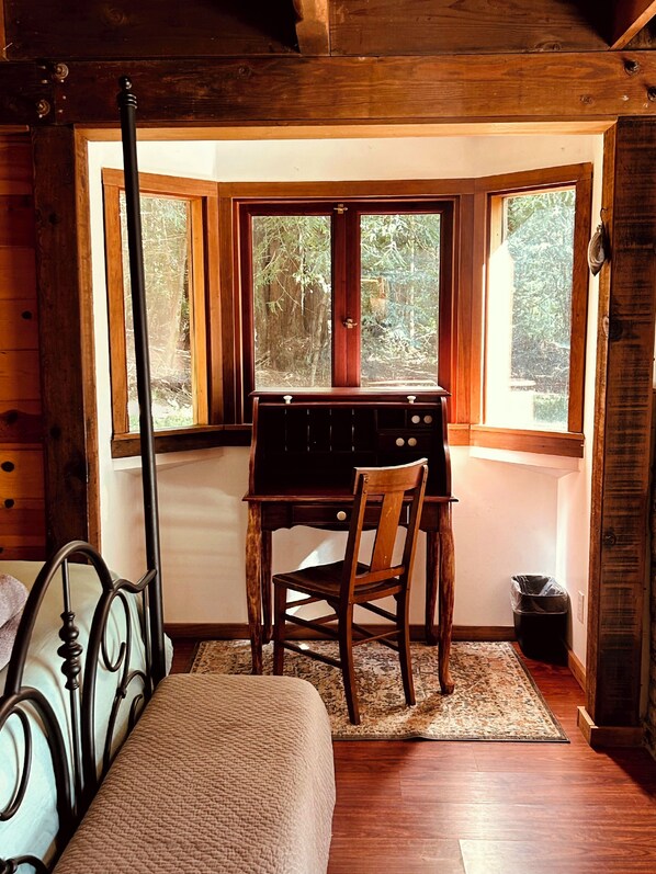 A wooden cabin room with a bed, a desk, and a chair.