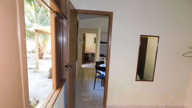 A room with a bed, a small table, and a chair. There is a door leading to a hallway with a view of the outside. - Simple house in Cabo Frio near the beach (Cabo Frio)
