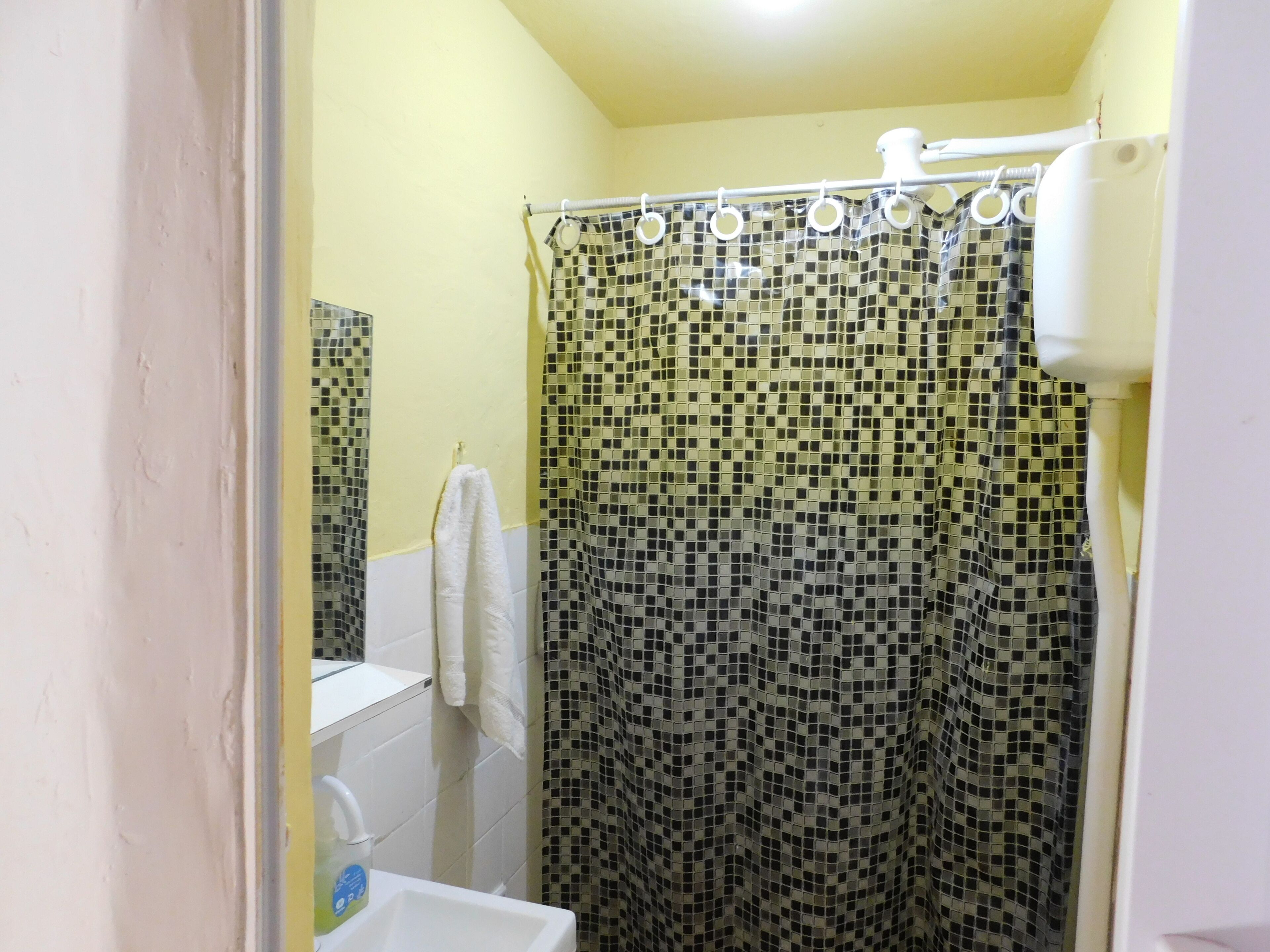 A bathroom with a shower curtain, a white towel hanging on the wall, and a sink with a soap dispenser.