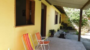 A covered outdoor seating area with two striped chairs, a concrete floor, and potted plants. - Simple house in Cabo Frio near the beach (Cabo Frio)