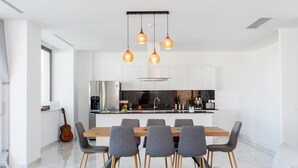 Een moderne keuken met een centraal eiland, een eethoek met een houten tafel en grijze stoelen, en hanglampen.