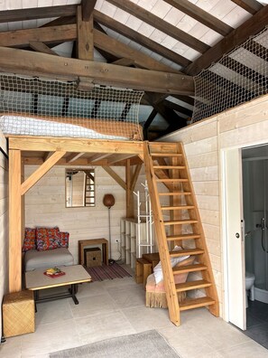 Une chambre à coucher aménagée dans un espace ouvert, avec une échelle en bois, un canapé et une petite table.