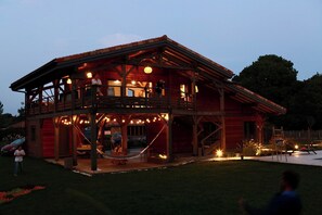 Une maison en bois à deux étages, dotée d’un balcon et d’un espace extérieur aménagé pour s’asseoir.