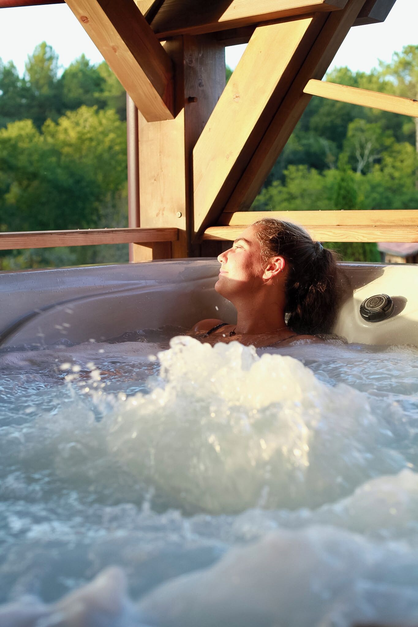 A person relaxing in a hot tub with a wooden structure overhead.