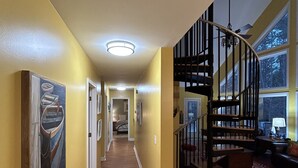 A hallway with wooden flooring, yellow walls, and a spiral staircase. There are framed pictures on the walls and a red patterned rug on the floor. - Lake Hartwell on McKinney Point, near Clemson! (Westminster)