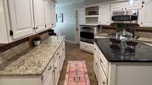 A kitchen with white cabinets, granite countertops, a central island, a microwave, and a stove. - Entire Spacious, Cozy home with backyard retreat (Norman)
