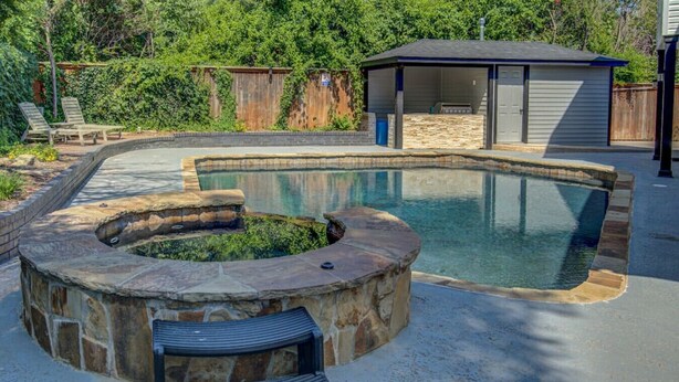 A swimming pool with a stone surround, a covered seating area, and a small shed in a backyard. - Entire Spacious, Cozy home with backyard retreat (Norman)