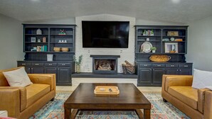 A living room with dark wood cabinets, a fireplace, a flat-screen TV, and two leather sofas. - Entire Spacious, Cozy home with backyard retreat (Norman)