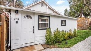 A white single-story house with a number 705 on the door, a small front yard with green shrubs, and a brick pathway leading to the door. - Downtown CDA Tiny House-Walk to the Lake (Coeur d'Alene)