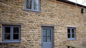 Un bâtiment en pierre avec trois fenêtres et une porte, un banc et un vélo.