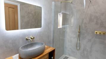 A modern bathroom with a large, speckled vessel sink, a wooden vanity, a glass-enclosed shower, and a mirror above the sink.