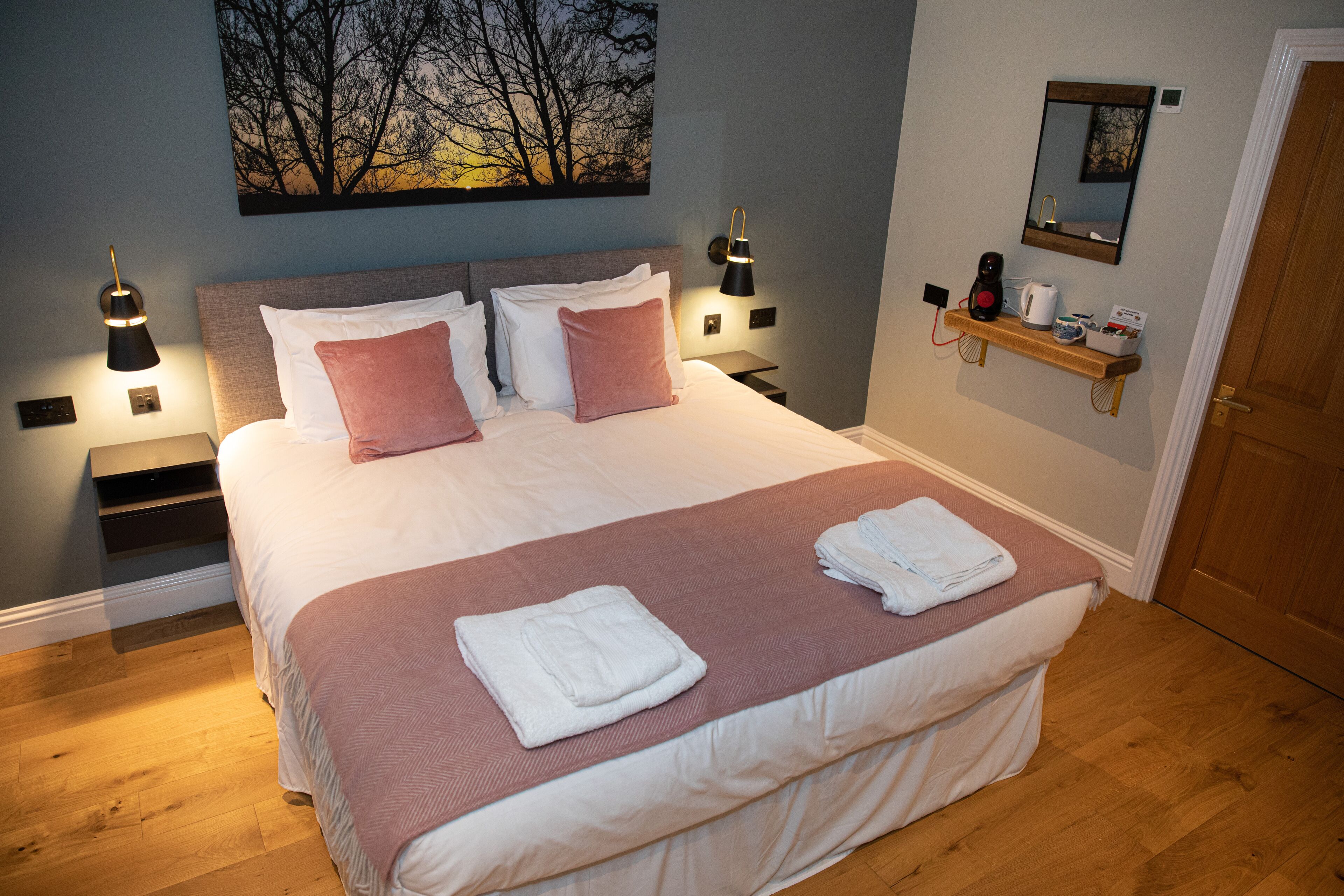 Una cama bien hecha con almohadas rosas y blancas, un cabecero de madera y una mesita de noche con una lámpara.