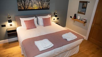 Una cama bien hecha con almohadas rosas y blancas, un cabecero de madera y una mesita de noche con una lámpara.