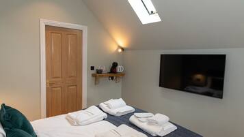 Een slaapkamer met een bed, een houten deur, een plank met toiletartikelen en een flatscreen televisie aan de muur.