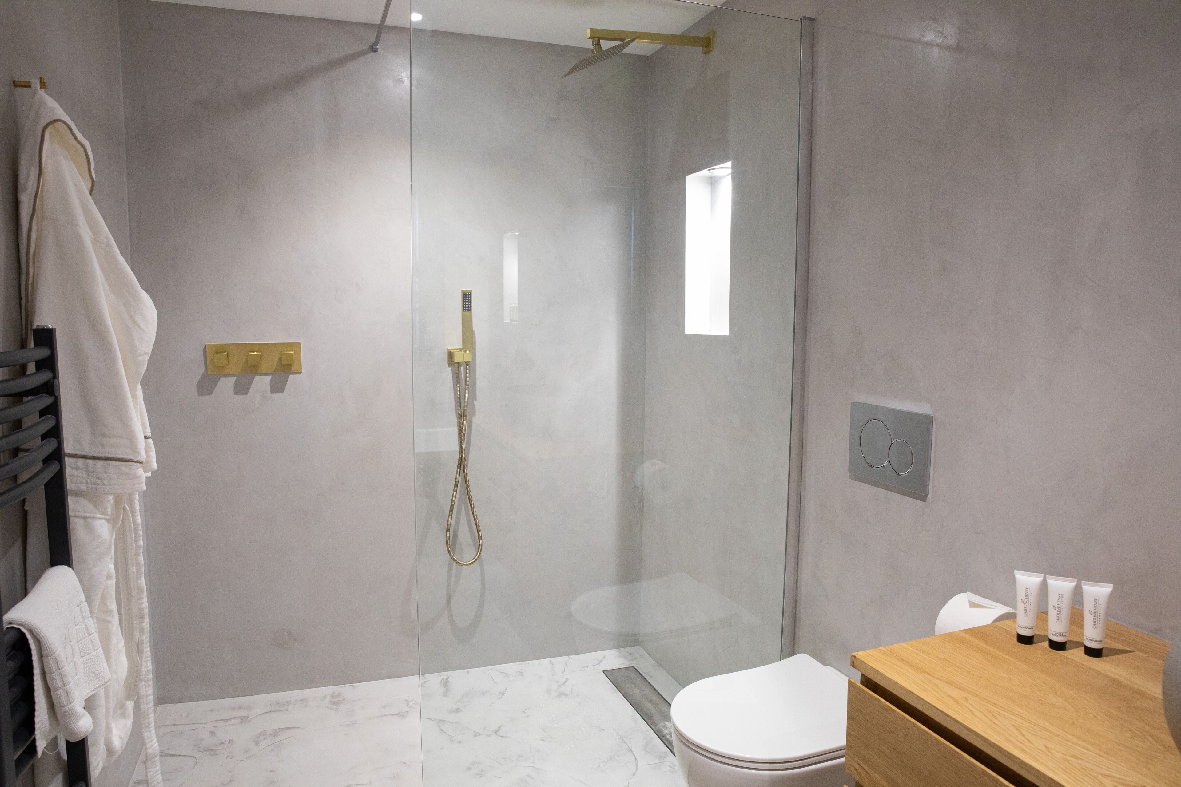 A modern bathroom with a glass-enclosed shower, a wooden vanity with toiletries, and a marble floor.