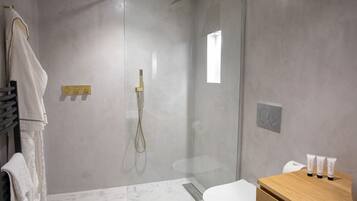 A modern bathroom with a glass-enclosed shower, a wooden vanity with toiletries, and a marble floor.