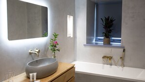 Une salle de bain moderne avec un grand lavabo rond, un miroir, une fenêtre avec une plante et une baignoire.
