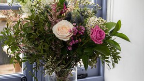 Un vase en verre transparent, contenant un bouquet de fleurs, est posé sur un rebord de fenêtre, à côté d’une pile de livres.