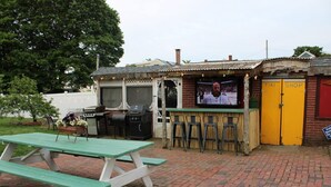 Area bar all'aperto con griglia, posti a sedere e schermo televisivo.