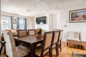 Un comedor con una mesa y sillas de madera, un televisor montado en la pared y un cuadro enmarcado sobre la mesa.