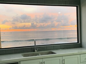 Eine Küche mit einem großen Fenster mit Blick auf einen Sonnenuntergang über dem Meer.