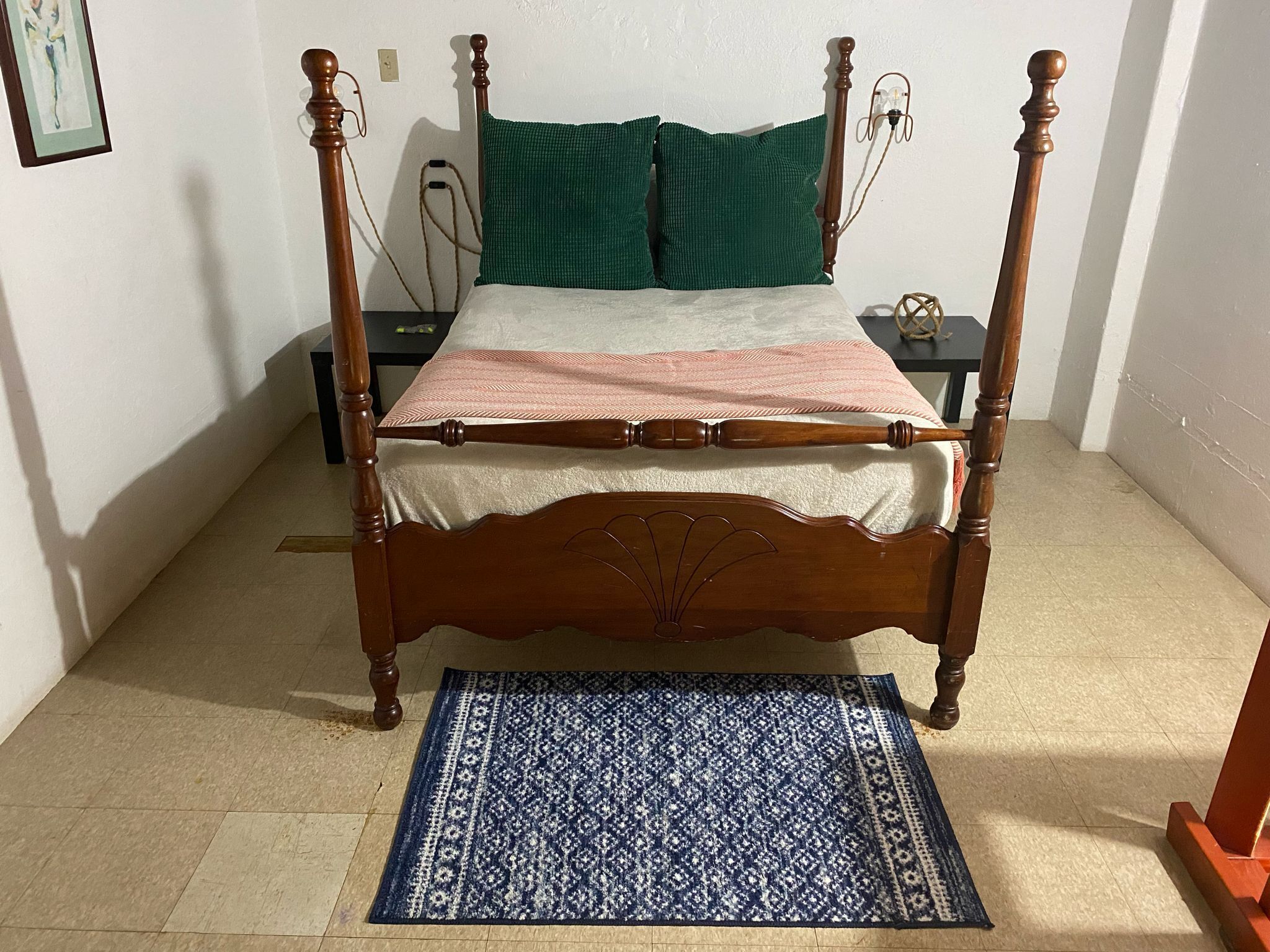 A four-poster bed with a wooden frame, a green pillow, and a patterned bedspread.