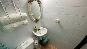 A bathroom with a toilet, sink, and mirror. There are towels and a trash bin.