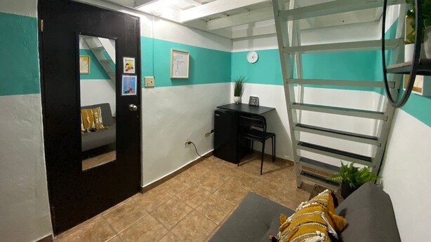 A room with teal and white walls, a black door, a desk with a chair, a ladder, and a sofa with a patterned cushion.