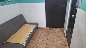 A small, enclosed room with a grey sofa and a brown tiled floor.