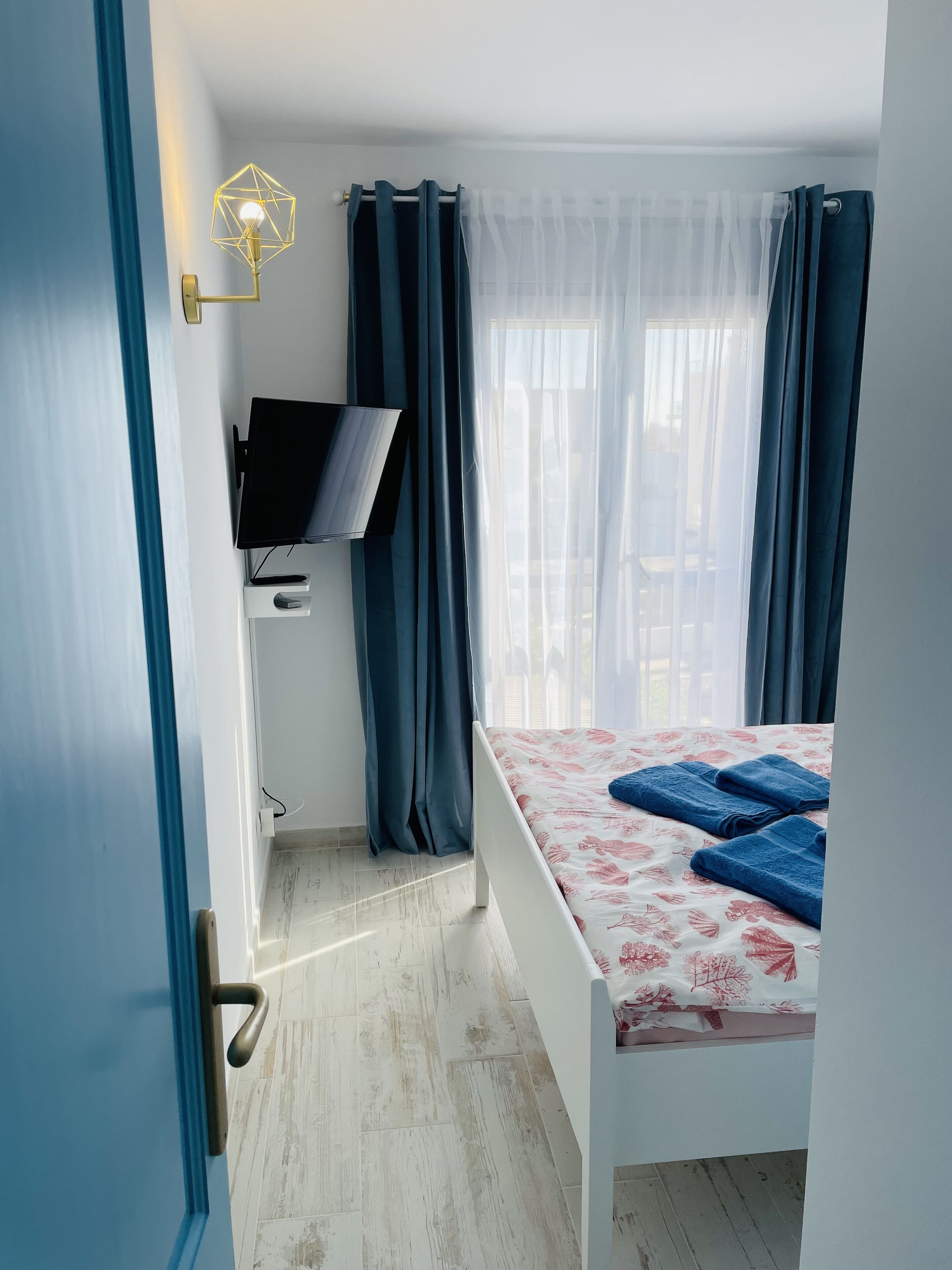 A bedroom with a bed, a TV, and a window with curtains.