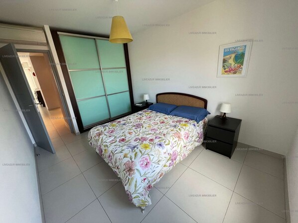 A bedroom with a bed, nightstands, a lamp, a sliding door, and a poster on the wall.