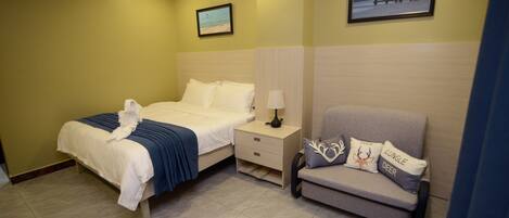 Una habitación de hotel con cama, mesita de noche, sofá y dos cuadros colgados.