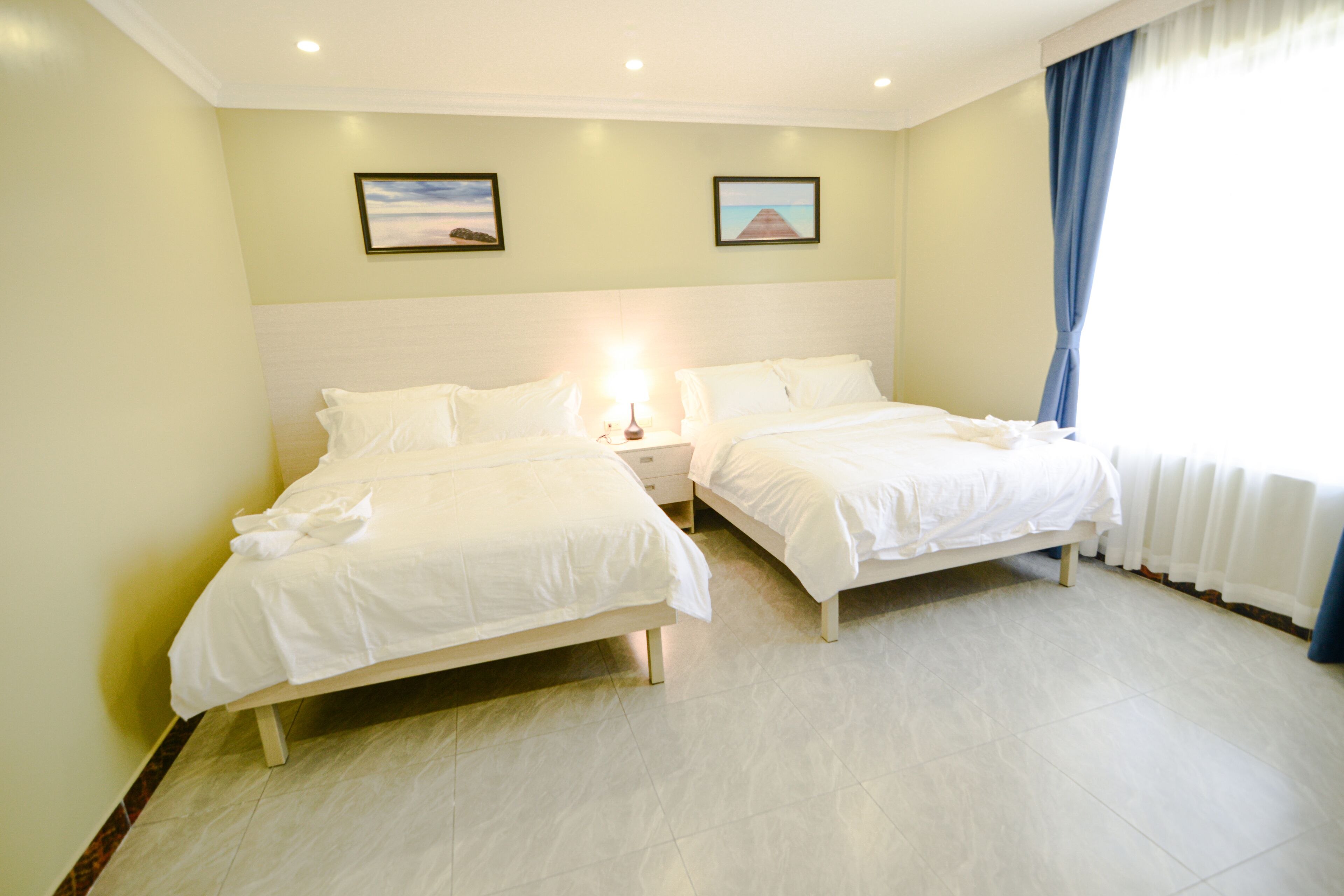 A hotel room with two beds, a nightstand, and a window with curtains.
