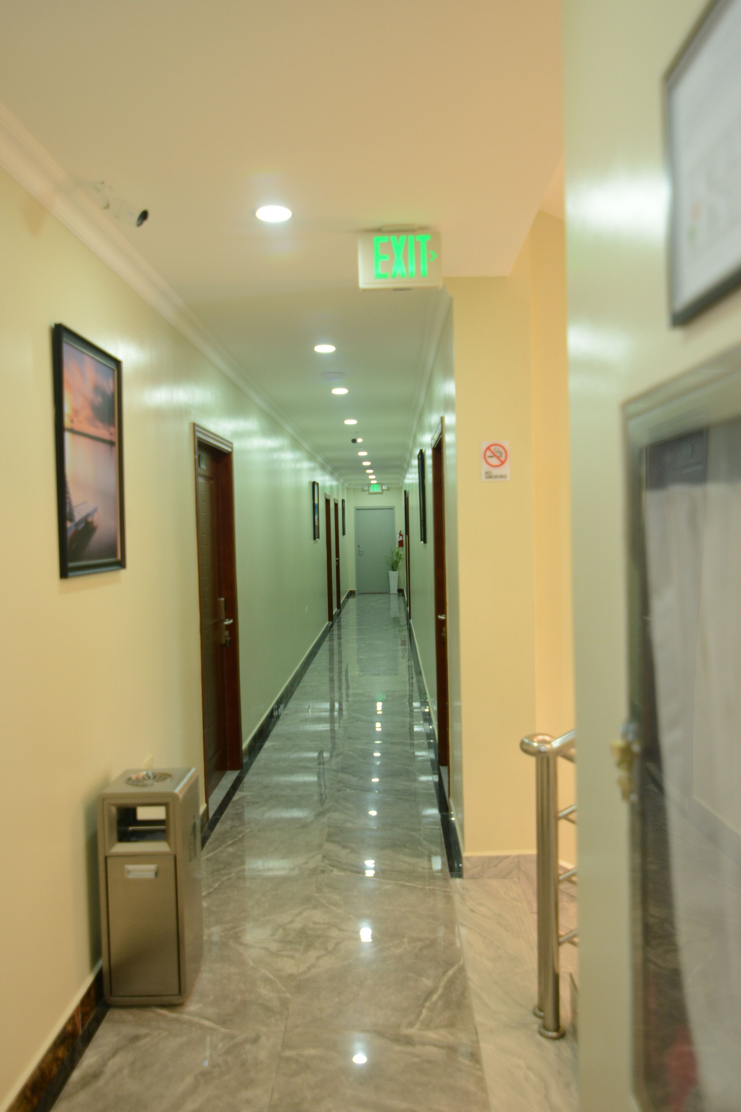 A hotel hallway with a marble floor, framed pictures on the walls, and a trash bin.