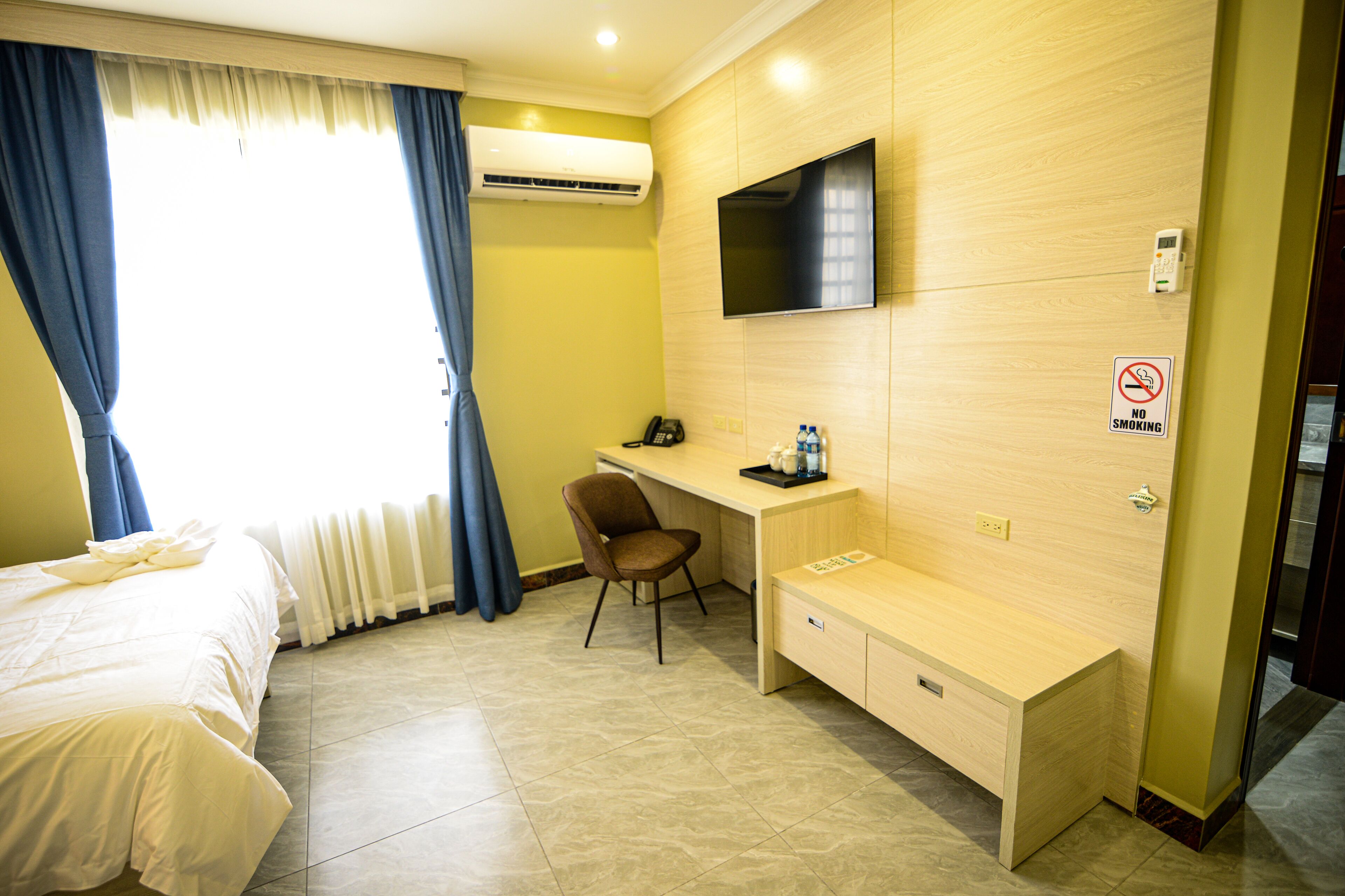 Habitación de hotel con cama, escritorio, silla, televisor montado en la pared y cartel de prohibido fumar.