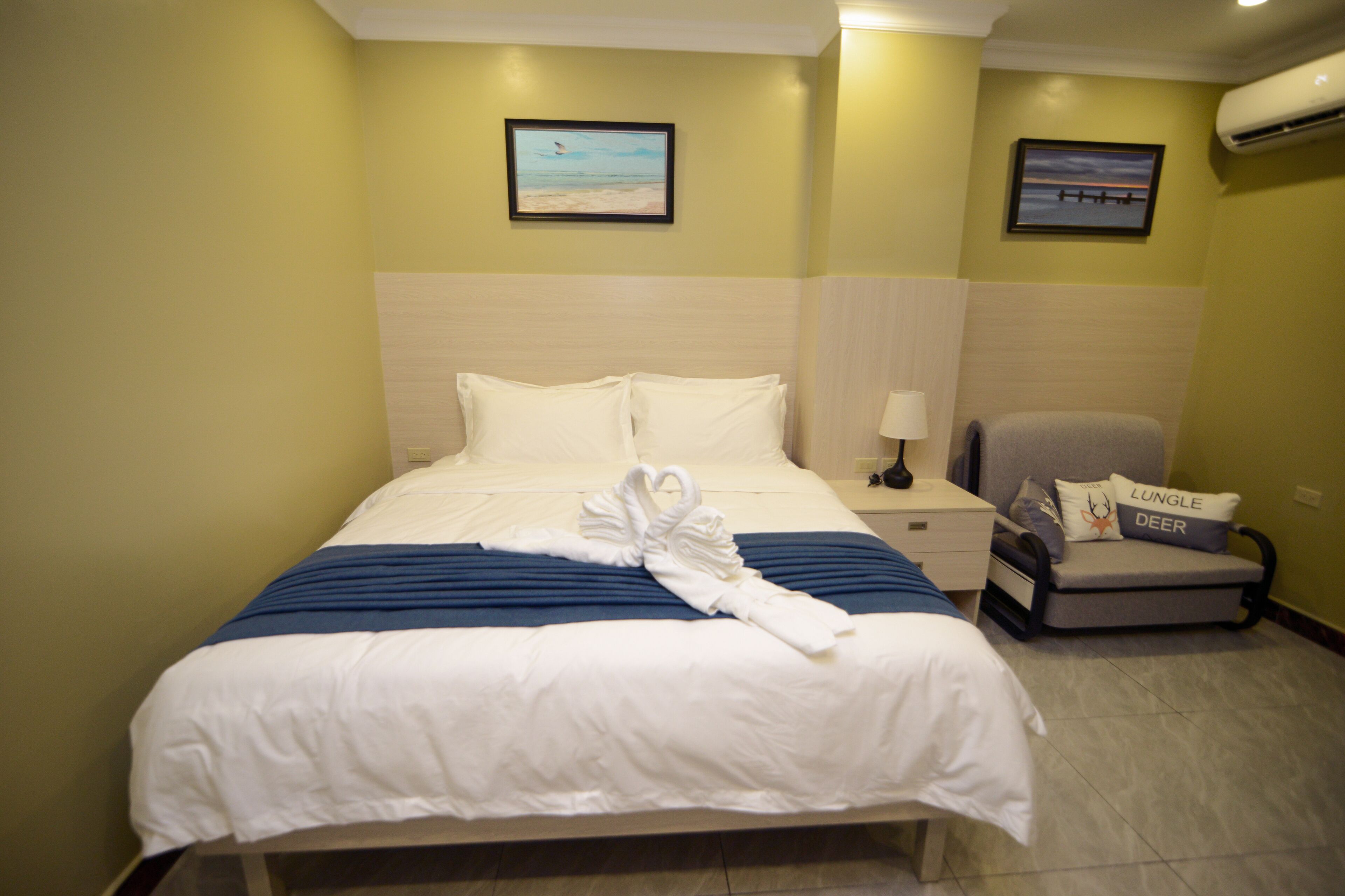 A hotel room with a bed, a nightstand, a chair, and two framed pictures on the wall.