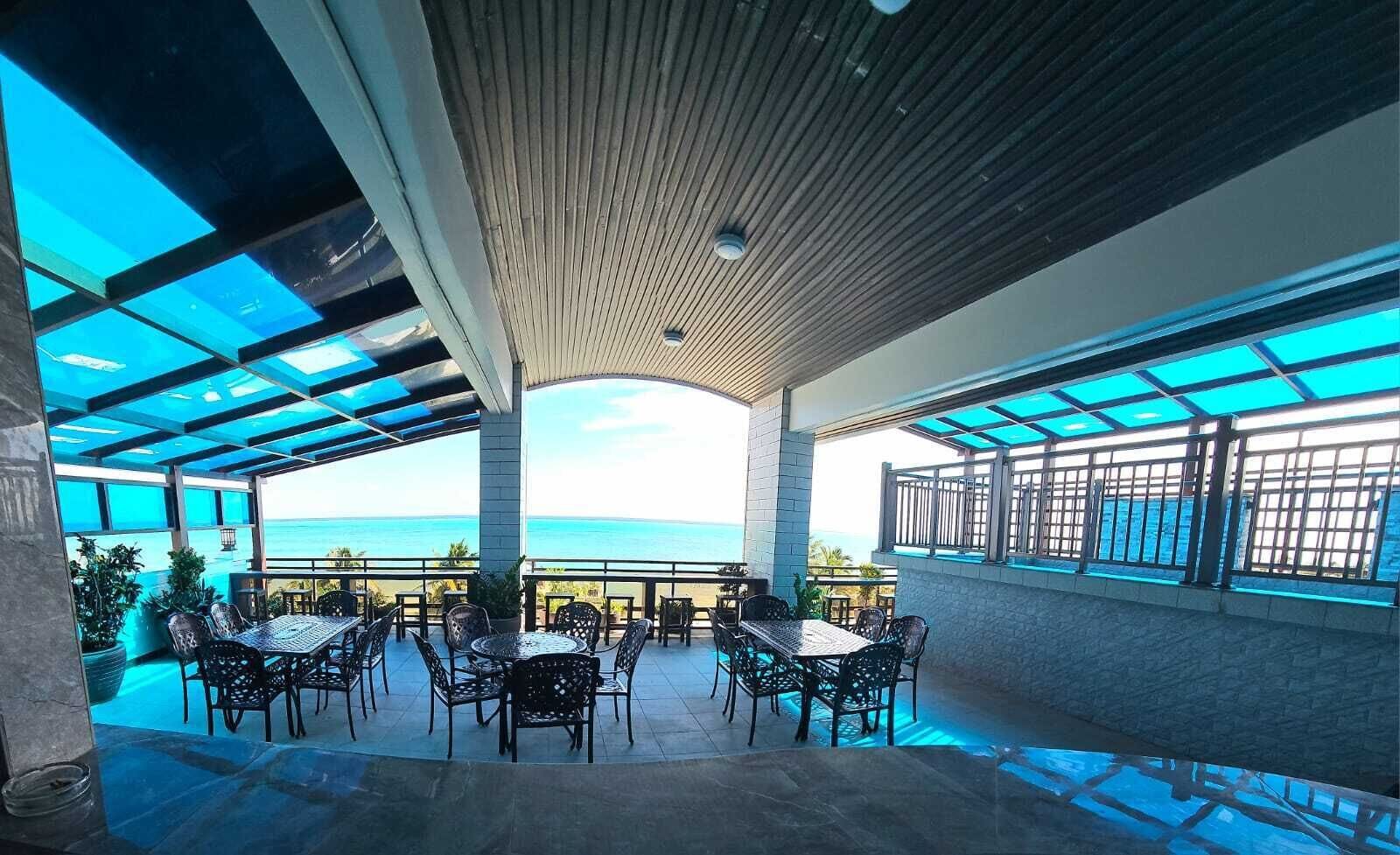 A covered outdoor seating area with tables and chairs, overlooking a scenic ocean view.