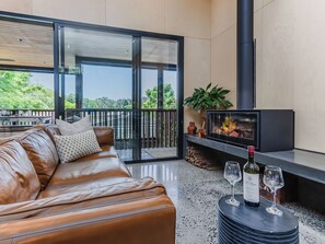 Ein modernes Wohnzimmer mit einer Ledersofa, einem Kamin, einem Fernseher und einem Balkon mit Blick auf Grünflächen.