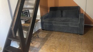 Una habitación con un sofá negro, una escalera de madera y un suelo de baldosas.